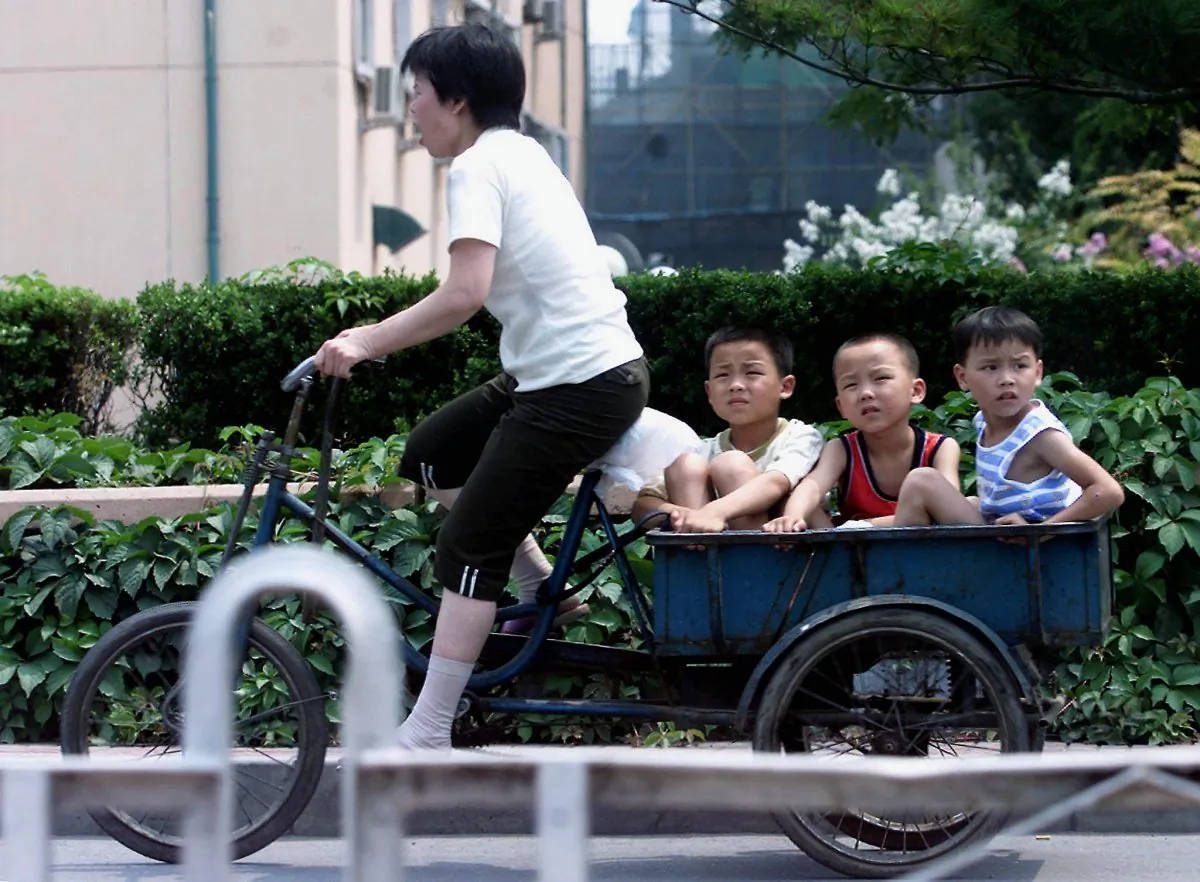 A woman peddles hard as she takes three young boys on her tricycle along a street in Beijing on July 18, 2001. (Goh Chai Hin/AFP/Getty Images)