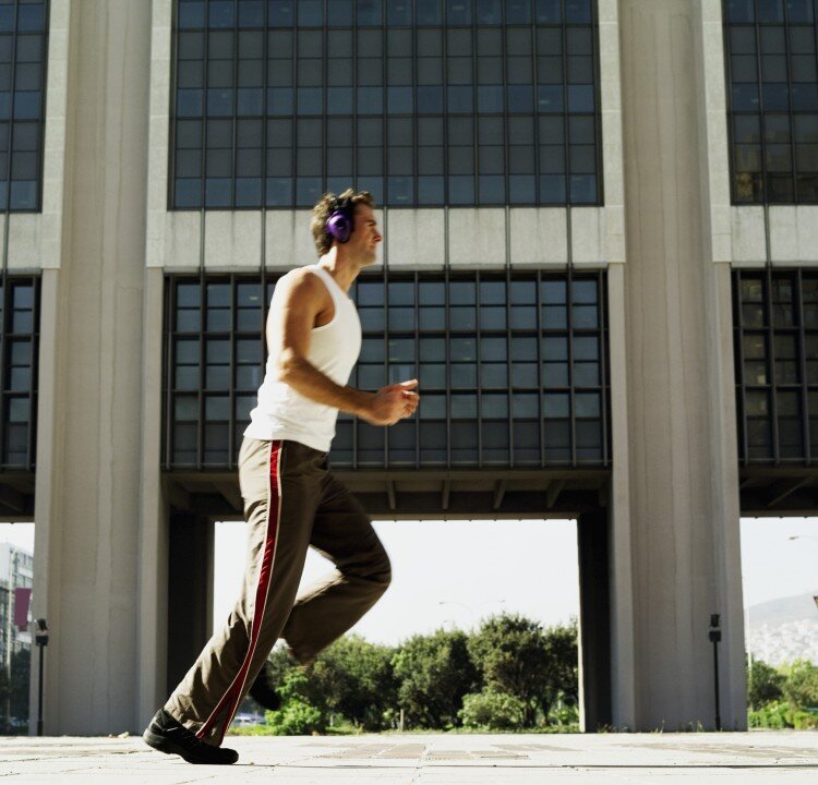 A man listens to music while jogging. Using noise-reduction headphones that dampen outside sound will allow you to keep the volume low and help to protect your hearing. (Stockbyte/Photos.com)