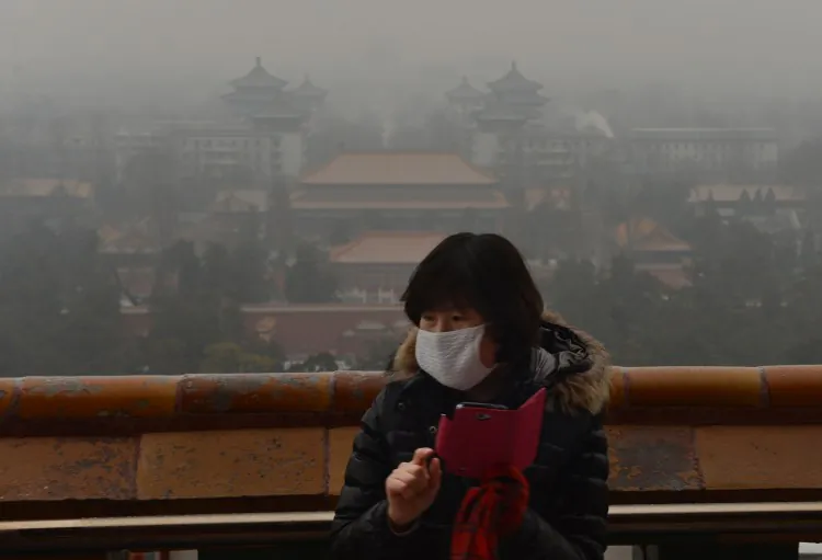 A Chinese tourist takes photos from historic Jingshan Park as smog continues to shroud Beijing on Jan. 31. A recent report says Beijing is suffering overpopulation. (Mark Ralston/AFP/Getty Images)