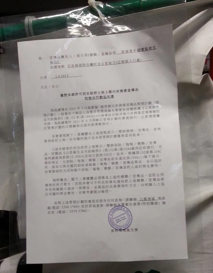 A Hong Kong government notice placed on a banner belonging to the Hong Kong Youth Care Association, a communist front group, said that the exhibit was in violation of the law and had to be removed, lest the group face stiff fines. (Expose the Evil Deeds of the Hong Kong Youth Care Association)