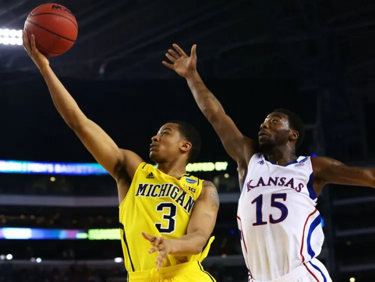 Trey Burke (L) drives past Elijah Johnson as the Michigan Wolverines shocked the Kansas Jayhawks with a late-game charge to send Kansas packing. (Tom Pennington/Getty Images)