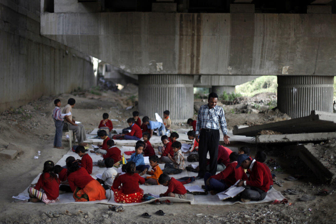 Rajesh Kumar, the founder of a free school for slum children, teaches a class at a free school for impoverished children under a mass transit bridge in New Delhi, India on March 13, 2013. Kumar fears his project is precarious. He needs more volunteer teachers because of the mass of students, but doesn't know where to find them. And his unregistered school is squatting on railroad property. "Whenever I am asked to leave this place, I will have to," he said. "Right now, the children are studying. We will take each day as it comes. As long as it remains possible, let's take advantage of it." (AP Photo/Altaf Qadri)