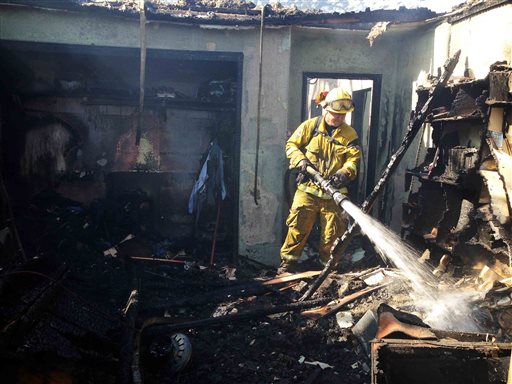 A firefighter puts out the remaining hot spots in the one building that has burned as a result of a brush fire burning in the hills above Banning, Calif., on Wednesday, May 1, 2013. (AP Photo/The Press-Enterprise, Terry Pierson)