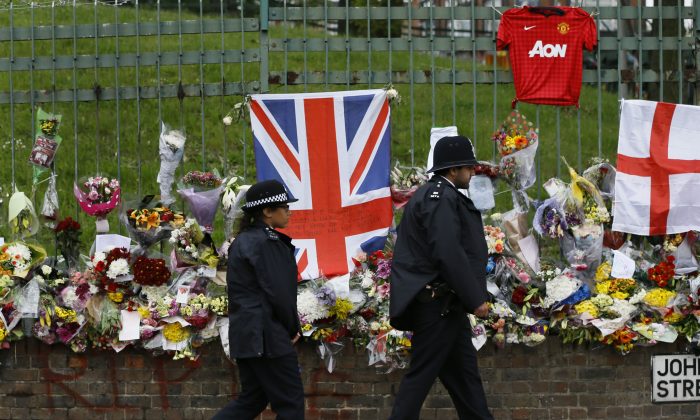 British police officers walk past some of the thousands of tributes left in honour of murdered 25-year-old British soldier Lee Rigby, near Woolwich Barracks in London, Wednesday, May 29, 2013. An autopsy shows that an off-duty soldier killed in a suspected Islamic extremist in London attack last week died from multiple cuts and stab wounds after he was hit by a car, police said Wednesday. (AP Photo/Lefteris Pitarakis)