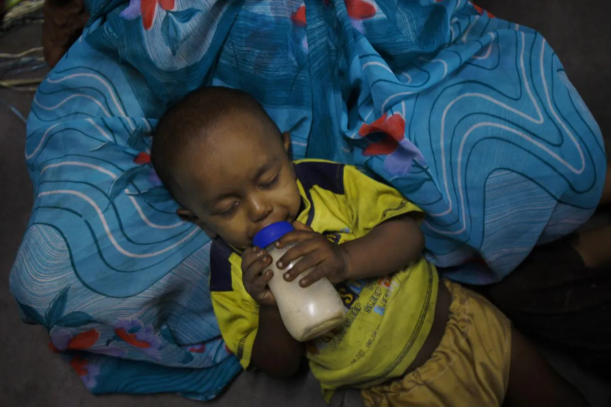 An underprivileged Indian child, drinks milk lying on the lap of a helper at Apnalaya, a voluntary organization which provides free meals to children of economically challenged parents in Mumbai, India, Monday, April 15, 2013. (AP Photo/Rafiq Maqbool)