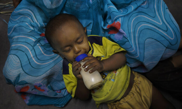 An underprivileged Indian child, drinks milk lying on the lap of a helper at Apnalaya, a voluntary organization which provides free meals to children of economically challenged parents in Mumbai, India, Monday, April 15, 2013. (AP Photo/Rafiq Maqbool)