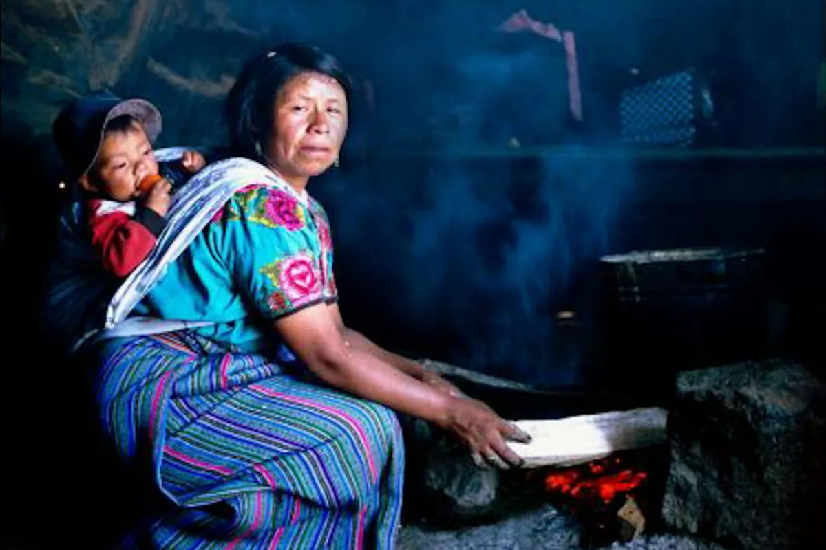 A woman in Guatemala cooks over an open fire with her child swaddled to her back. (Courtesy Nigel Bruce)