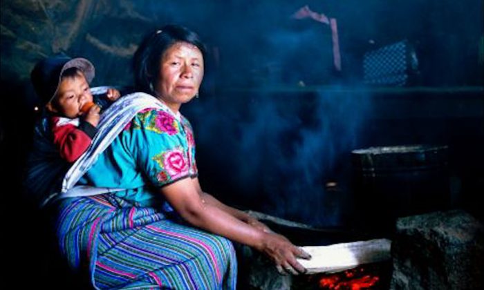 A woman in Guatemala cooks over an open fire with her child swaddled to her back. (Courtesy of Nigel Bruce)