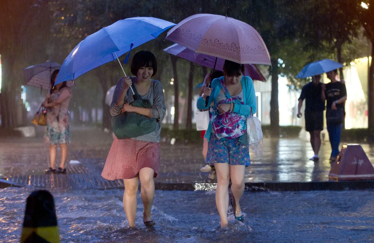 Two women cross a flooded street during heavy rainfall in Beijing on July 21, 2012. Beijing is installing nets in up to 1,000 manholes to prevent people from falling in when covers are removed, by either thieves or floodwaters. (Ed Jones/AFP/Getty Images)