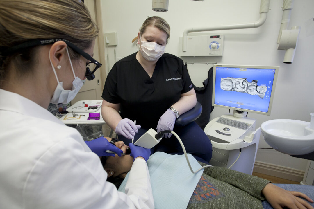 Clinical coordinator Wioletta Lazarz (R) assists Dr. Julie Hassid with patient Alicia Mootoo. A camera is inserted in her mouth that generates a scan of each tooth's contours. (Samira Bouaou/The Epoch Times)
