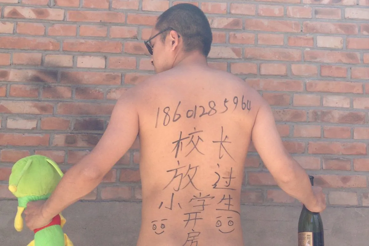 Beijing-based poet Wang Zang poses at his workplace in Beijing with the Chinese characters “Principal, get a room [with me]. Leave the young students alone.” scribbled on his back while holding a stuffed animal and a liquor bottle, on May 29, 2013. Artists, activists, university students, and police officers are photographing themselves—some nude and provocatively posed, some angry and menacing—with the same message. (AP Photo/Courtesy of Wang Zang)