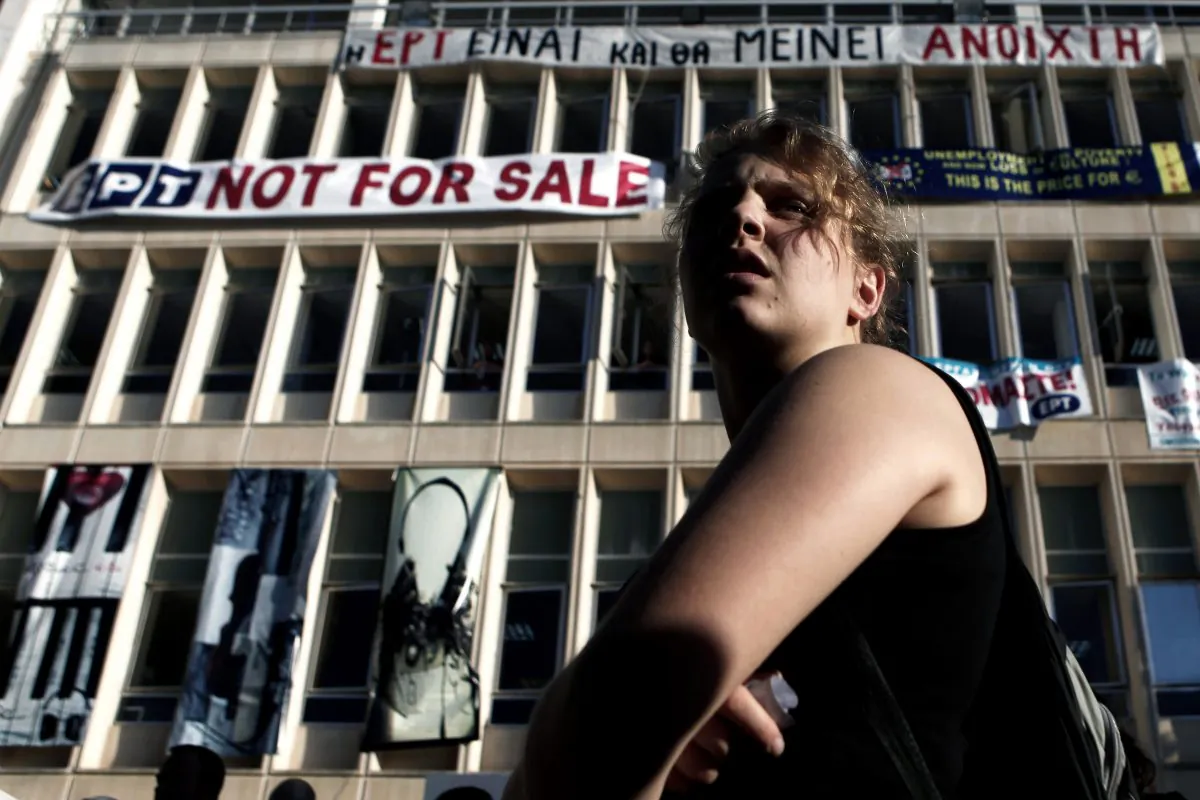 A protester stands in front of the Greek state television ERT headquarters in Athens on June 18, 2013. The banner in Greek language on the top reads, "ERT is, and will remain open." (AP Photo/Petros Giannakouris)