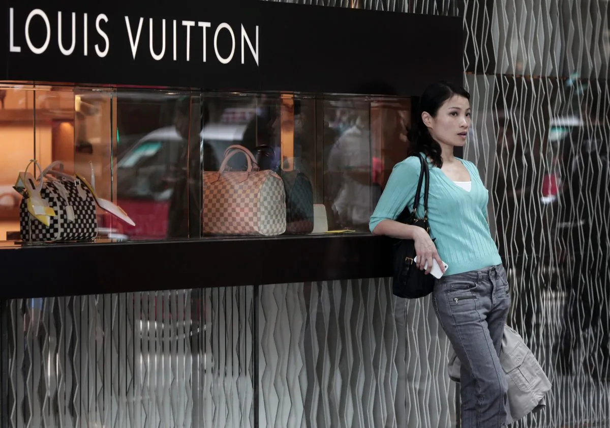 In this file photo, a Chinese woman leans on a Louis Vuitton shop display window in Hong Kong, on April 23, 2013. While cashed-up Chinese who travel to the Hong Kong for luxury shopping, the poorest 5 percent of Chinese households live on US$163 per year. (Anthony Wallace/AFP/Getty Images)