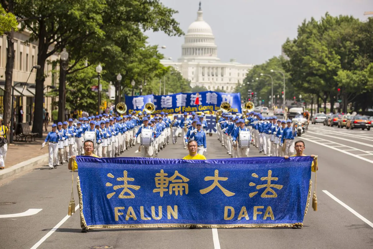 Three Falun Dafa practitioners lead the Divine Land Marching Band with a blue and gold banner. Adherents of the practice march down from 3rd & 4th Street to the Monument in Washington, D.C. on July 18. (Edward Dai/Epoch Times)