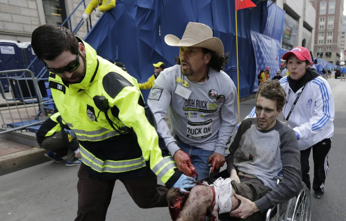 In this Monday, April 15, 2013 file photo, an emergency responder and volunteers, including Carlos Arredondo, in the cowboy hat, push Jeff Bauman in a wheelchair after he was injured in one of two explosions near the finish line of the Boston Marathon. Dzhokar Tsarnaev, the suspect in the bombing who is still alive, goes to court for the first time on July 10, 2013. (AP Photo/Charles Krupa, File)