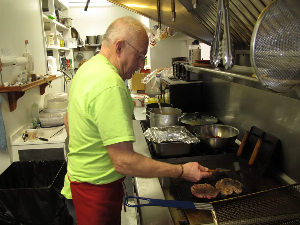 Sherman Sykes cooks hamburgers for a lunchtime crowd at his restaurant in Henryville, Ind., in this file photo. Restaurant Jobs made up the bulk of the growth in June. (Bruce Schreiner/AP)