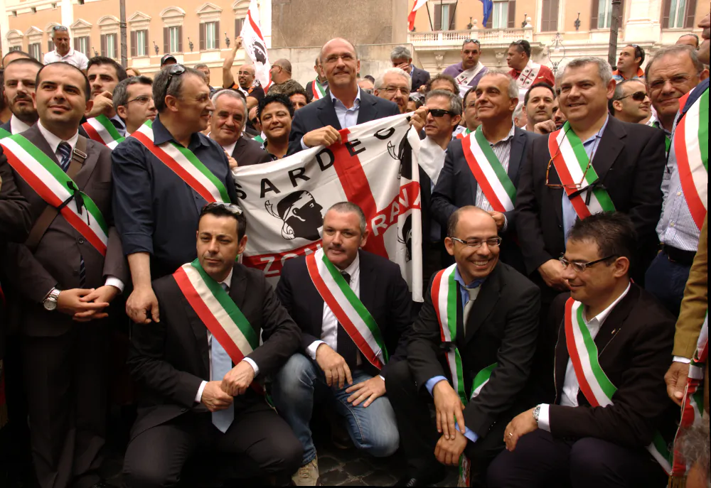 President of the Sardinian government Ugo Cappellacci (Center, holding flag) poses with Sardinian mayors to call for a free zone covering the island of Sardinia in front of the Italian parliament building on June 24, 2013. The island has become something of a poster child for the free zone economic solution to recession in Europe.(Andrea Lorini/Epoch Times)