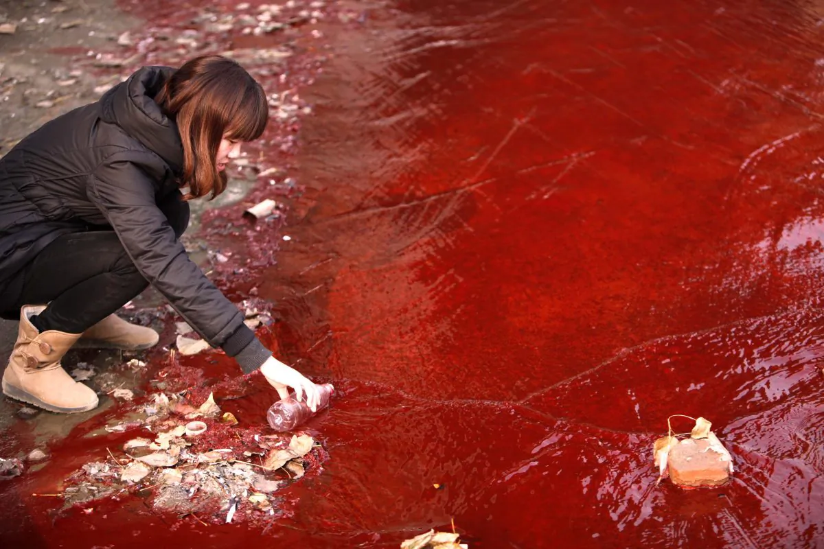 A woman collects a sample of the red polluted water flowing from a sewer into the Jian River in Luoyang, in central China's Henan Province, on Dec. 13, 2011. Pollution from a medicine factory in Daliuying Village in Henan Province creates a sour smell in the air, and makes underground water salty and unclear, state news media recently reported. (STR/AFP/Getty Images)