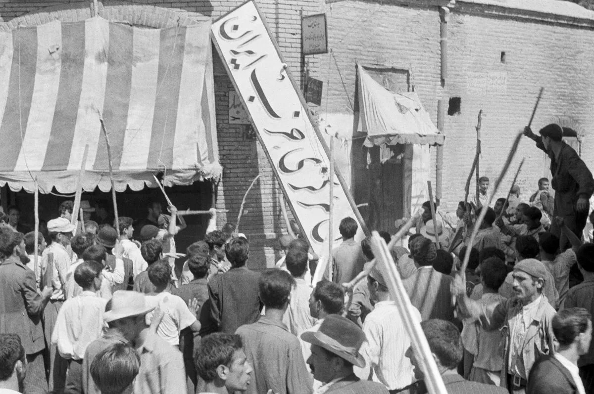 A crowd of demonstrators tear down the Iran Party's sign from the front of the headquarters in Tehran on Aug. 19, 1953, during the pre-Shah riot that swept through the capital and ousted Persian Prime Minister Mossadegh and his government. (AP Photo)