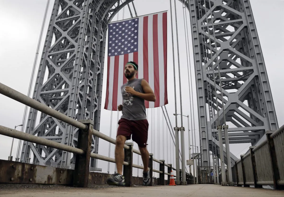 A runner passes under the largest free-flying American flag in the world over the George Washington Bridge Monday, Sept. 2, 2013, in Fort Lee, N.J. The flag flew on Labor Day under the upper arch of the bridge's New Jersey tower. (AP Photo/Mel Evans)