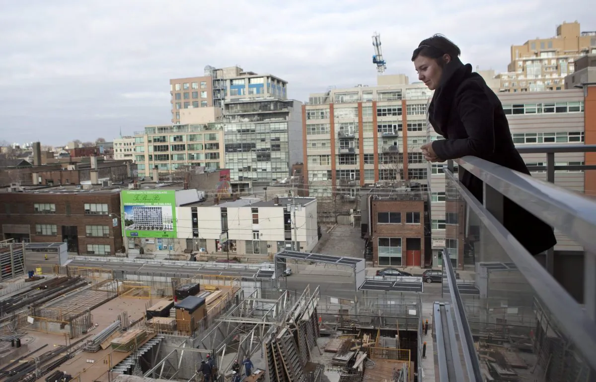 Condo owner Eva Kanovich looks onto a neighbouring condo under construction from her balcony in downtown Toronto in February 2012. The level of unsold new highrise condos remained large in recent months in the GTA, contributing to the fall in GTA housing starts in September reaching their lowest level in five months. (The Canadian Press/Pawel Dwulit)