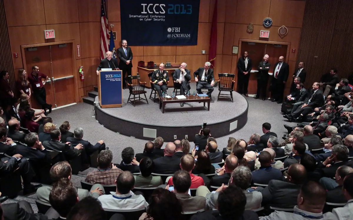 President of Fordham University the Rev. Joseph Michael McShane speaks at the International Conference on Cyber Security (ICCS), Aug. 8 at Fordham University in New York, while the directors of the NSA, CIA, and FBI are seated on stage. Chinese spies target conferences for espionage, due to the value of information available and high-level people who attend.(AP Photo/Bebeto Matthews)