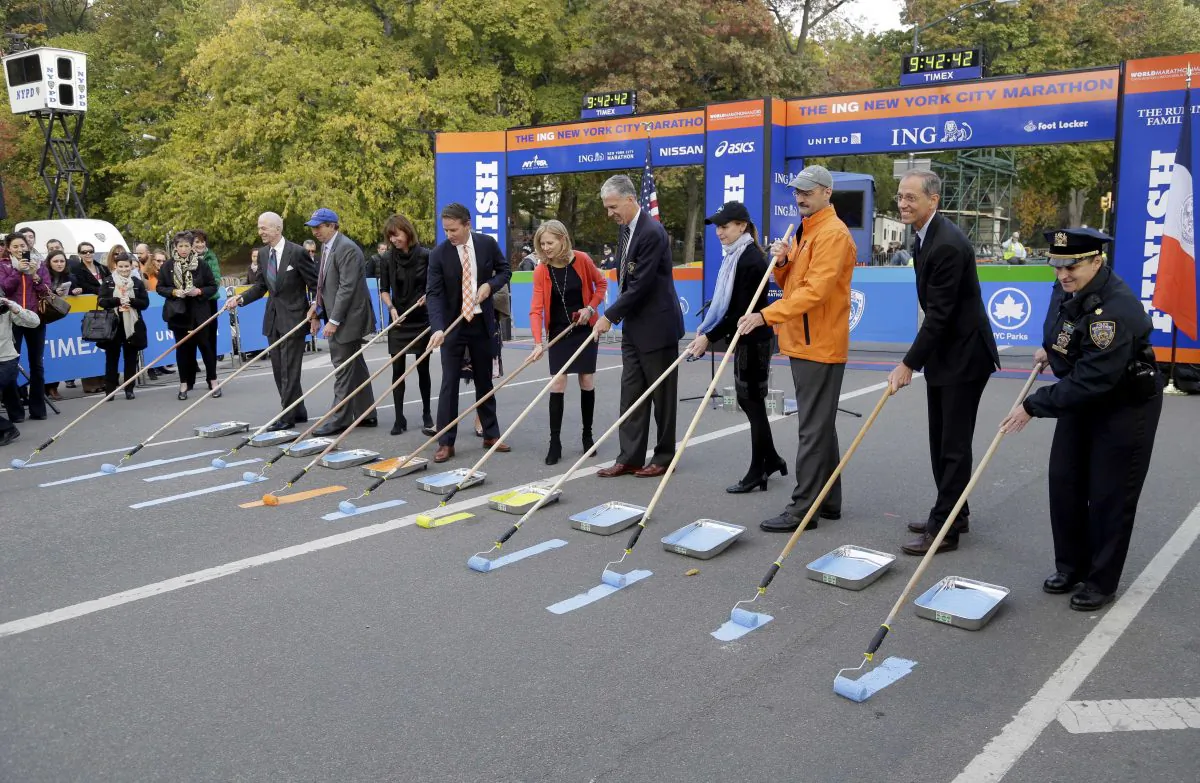 VIPs and officials, including Mary Wittenberg, New York Road Runners president and CEO (5th L), and Thomas Grilk, executive director of the Boston Athletic Association (6th L), participates in the ceremonial painting of the finish line of the NYC Marathon in Central Park, Oct. 30, 2013. (Seth Wenig/AP)