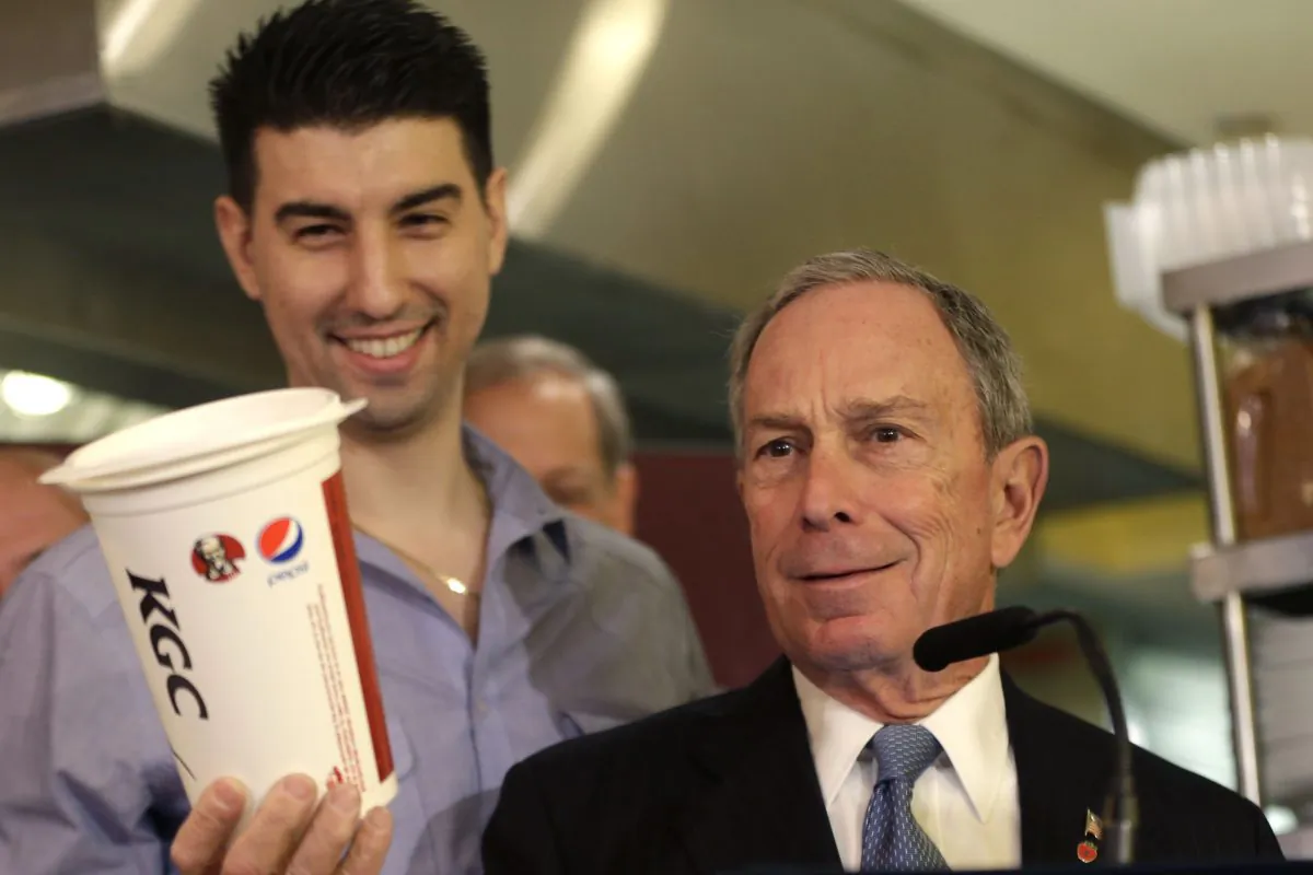 New York City Mayor Michael Bloomberg looks at a 64oz cup, as Lucky's Cafe owner Greg Anagnostopoulos (L), stands behind him. (Seth Wenig/AP)
