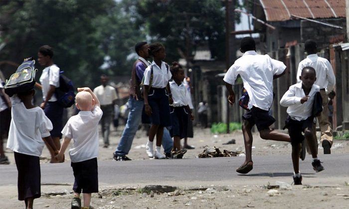 A young girl holds the hand of an albino boy as two other boys run across a road on their way back from school in Kinshasa, capital of Congo, Thursday Jan. 25, 2001. An article published in All Africa in October 2013 looks at the hardships an albino boy faces in the country, where the organs of albinos are hunted for witchcraft. (AP Photo/Christine Nesbitt)