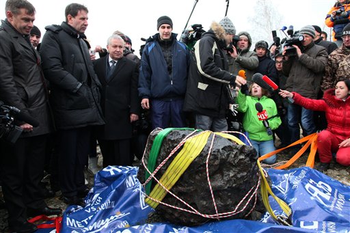 People look at what scientists believe to be a chunk of the Chelyabinsk meteor, recovered from Chebarkul Lake near Chelyabinsk, about 1500 kilometers (930 miles) east of Moscow, Russia, Wednesday, Oct. 16, 2013. Scientists on Wednesday recovered what could be the largest part of this meteor from Chebarkul Lake outside the city. They weighed it using a giant steelyard balance, which displayed 570 kilograms (1,256 pounds) before it broke. (AP Photo/Alexander Firsov)