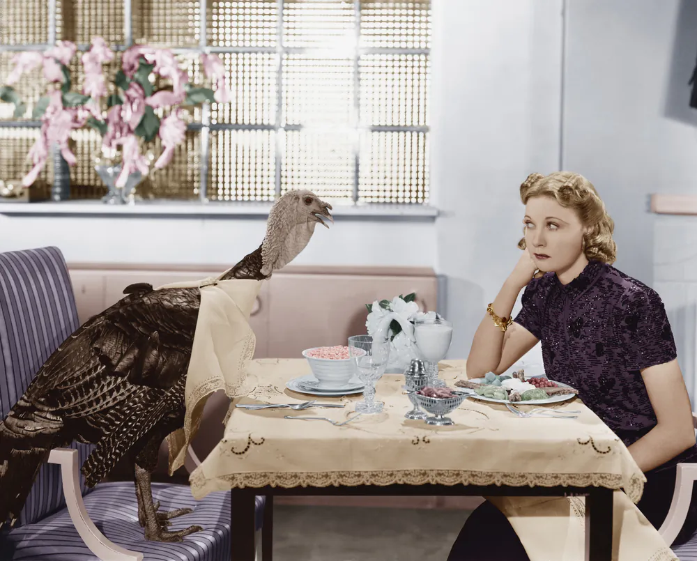 Woman eating meal at table with live turkey Image via Shutterstock*