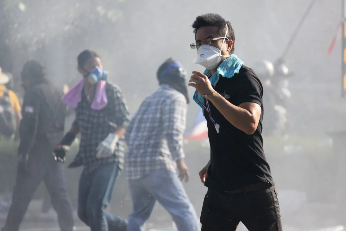 An anti-government protester flees tear gas and a water cannon during a bid to break through a police blockade near Thailand’s Government House on Dec. 1, 2013. (Cameron McKinley/Epoch Times)