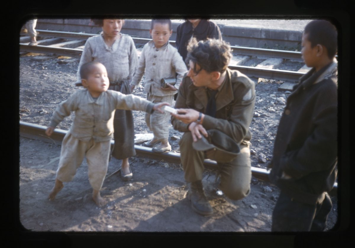 A Canadian gunner hands candy to a Korean boy at the rail yards in Tokchon, South Korea. (George Metcalf Archival Collection, © Canadian War Museum)