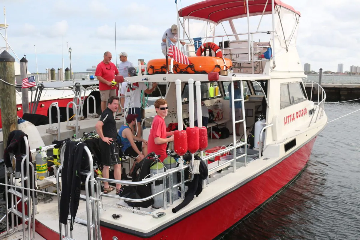 Captain David Brown standing on dock holding small yellow tank in red shirt, his grandson Al in foreground. Al is the third generation diver in the family. (Myriam Moran copyright 2014)