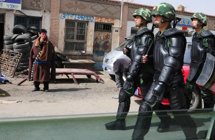 Chinese language signs are visible in this photo of a Tibetan man (L) in traditional clothing, watching as Chinese paramilitary troops in riot gear march along the streets of Guomaying, on the Tibetan plateau. Chinese policy appears aimed at replacing ethnic languages with Mandarin. (Frederic J. Brown/AFP/Getty Images)