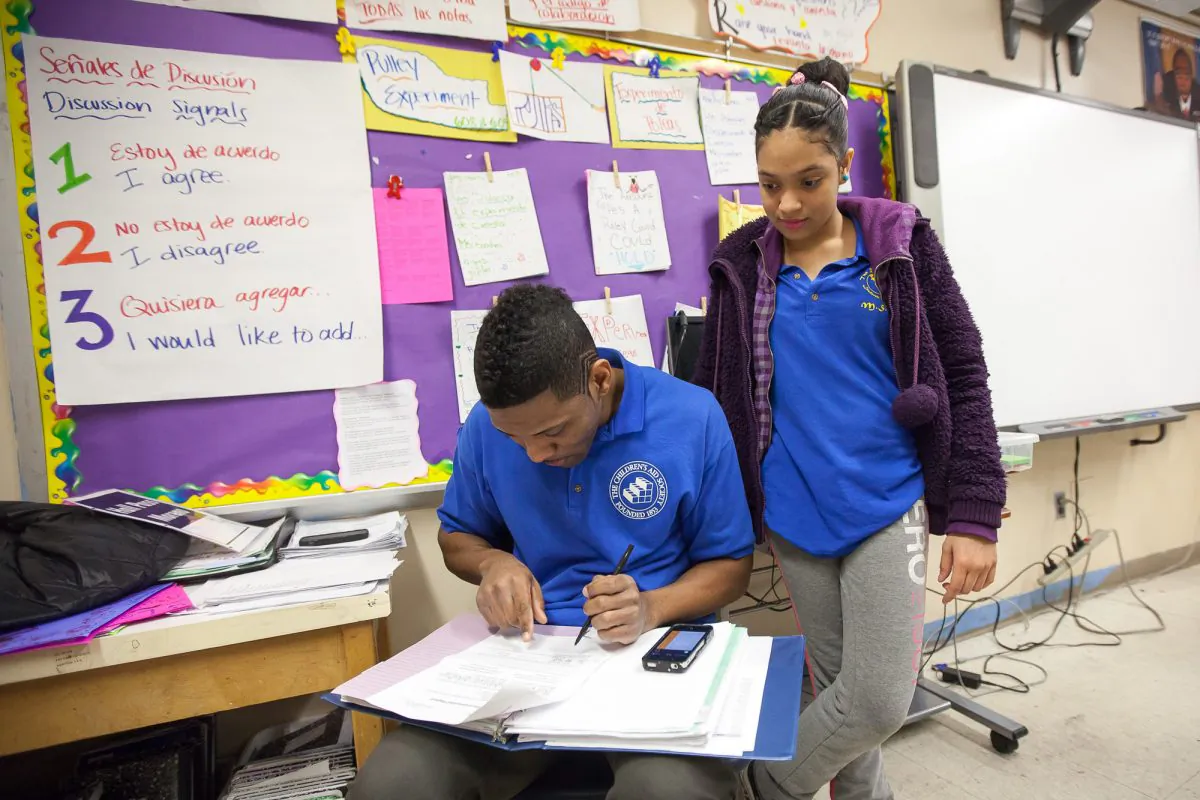 A student in a Children’s Aid Society leadership program helps another student complete his homework during an after-school study session at the Salomé Ureña de Henríquez Campus Community School, Manhattan, New York, Feb. 10, 2014. (Petr Svab/Epoch Times)