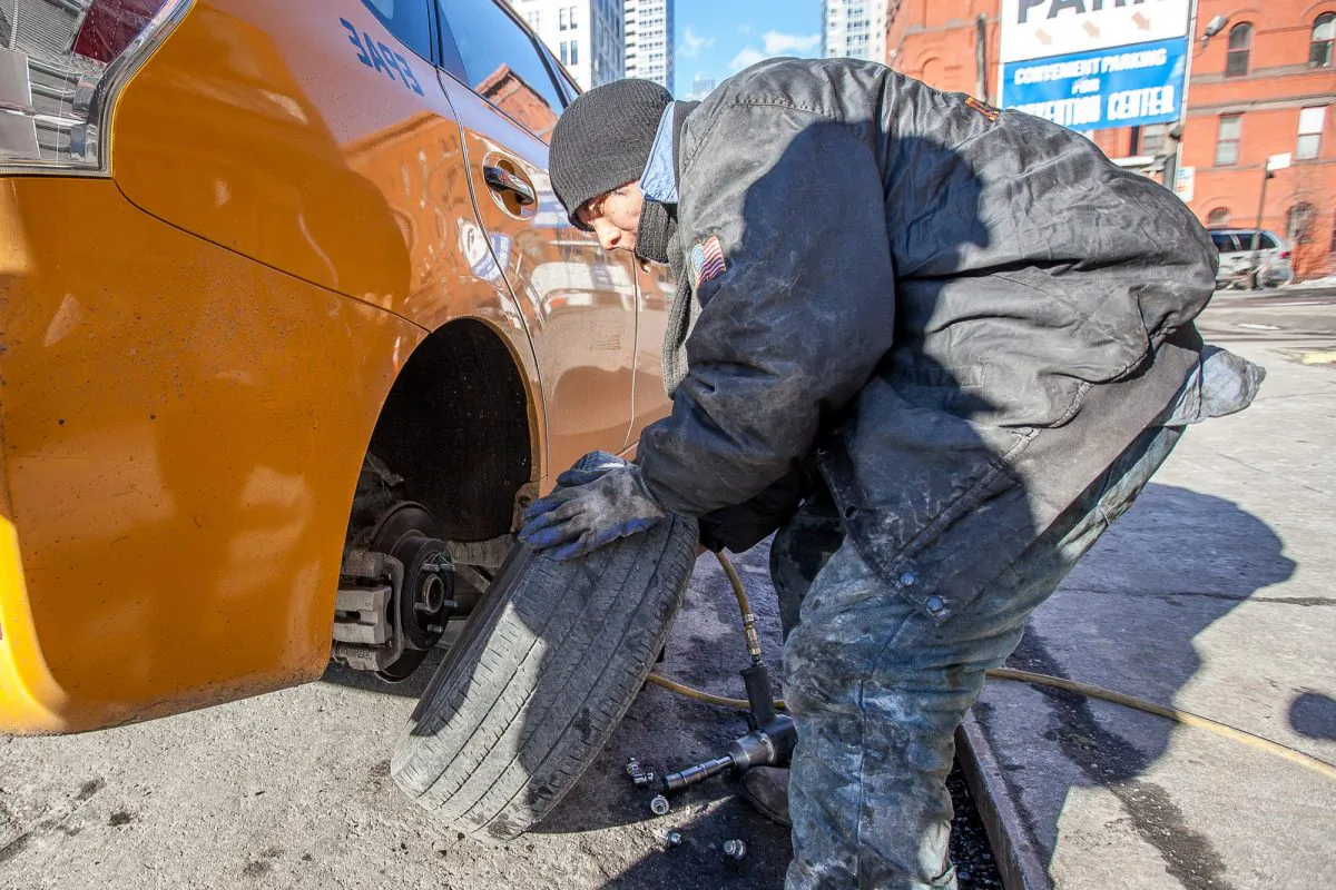 A man changes a flat tire on a taxi at a shop on 10th Avenue in Manhattan, New York, on Feb. 26, 2014. Damaged roads are costing each New York driver on average about $2,300 per year. (Petr Svab/Epoch Times)