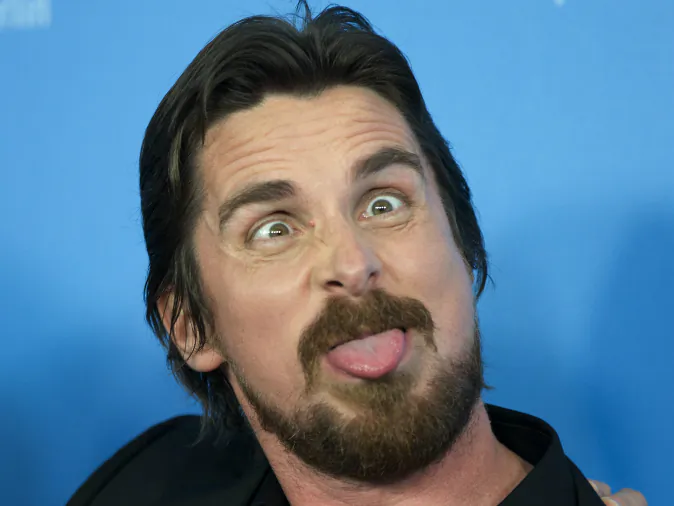 Actor Christian Bale pokes his tongue out at photographers during the photo call for the film American Hustle during the International Film Festival Berlinale, in Berlin, Friday, Feb. 7, 2014. (AP Photo/Axel Schmidt)