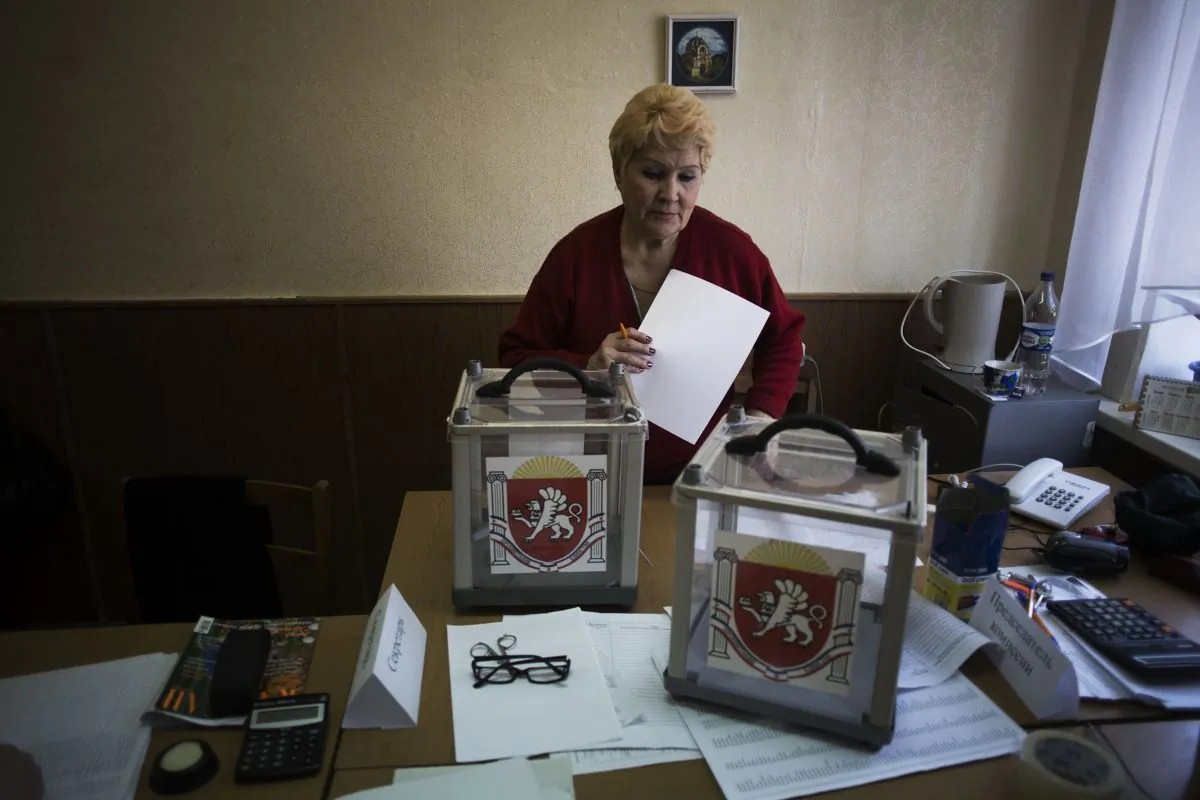 A Ukrainian woman, who is a member of the district electoral committee, makes final preparations as she stands next to ballot boxes for Sunday's referendum at a polling station in Simferopol, Ukraine, on March 15, 2014. Tensions are high in the Black Sea peninsula of Crimea, where a referendum is to be held Sunday on whether to split off from Ukraine and seek annexation by Russia. (AP Photo/Manu Brabo)