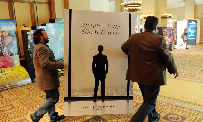 Sheldon Domke, left, and Adam Mast move an advertisement for the upcoming film "Fifty Shades of Grey" during the second day of  CinemaCon 2014 on Tuesday, March 25, 2014 in Las Vegas. The film is set for release Valentine’s Day of 2015. (Photo by Chris Pizzello/Invision/AP)