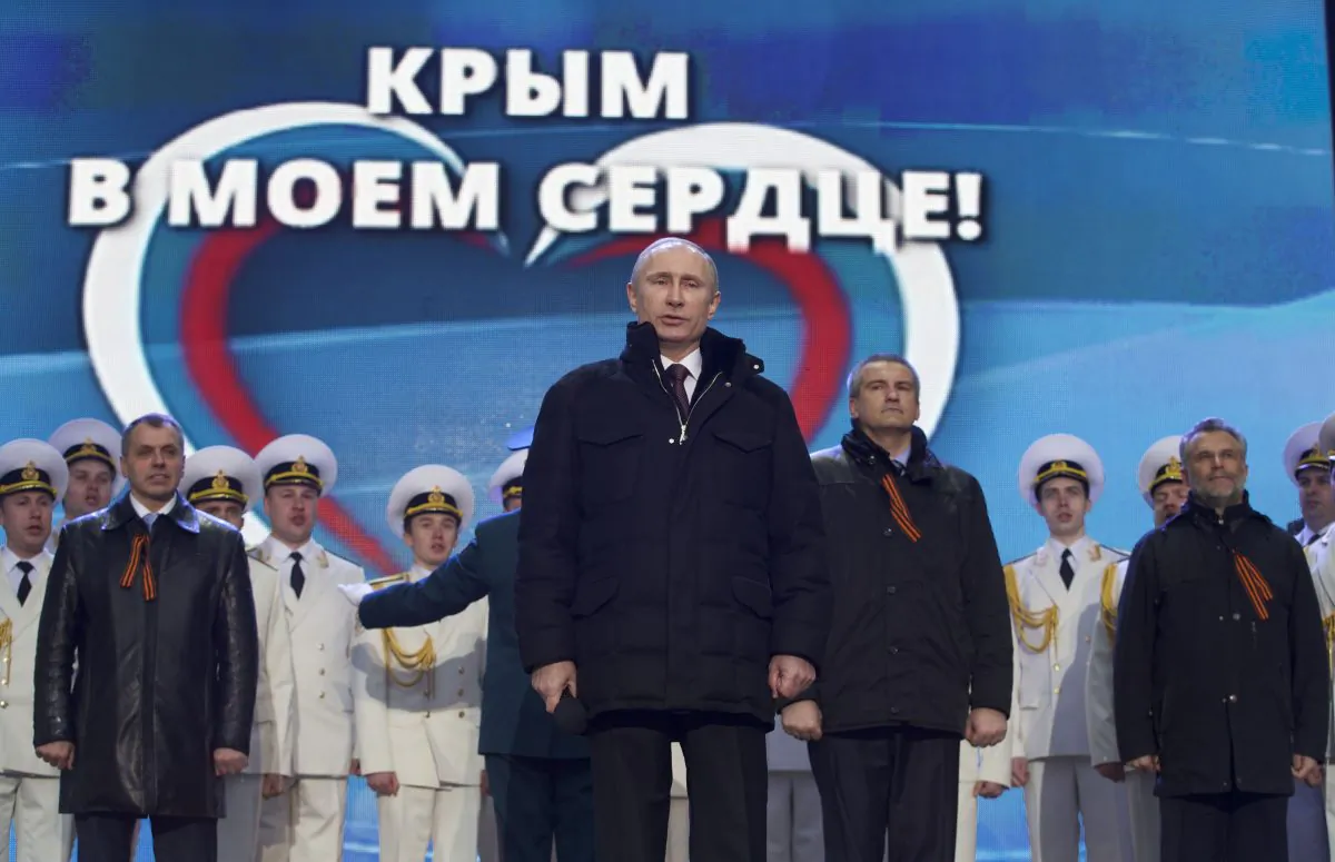 Russian President Vladimir Putin, with Crimean leaders in the background, sings the national anthem at a rally in support of Crimea joining Russia in Red Square in Moscow, Tuesday, March 18, 2014. (AP Photo/Pavel Golovkin)