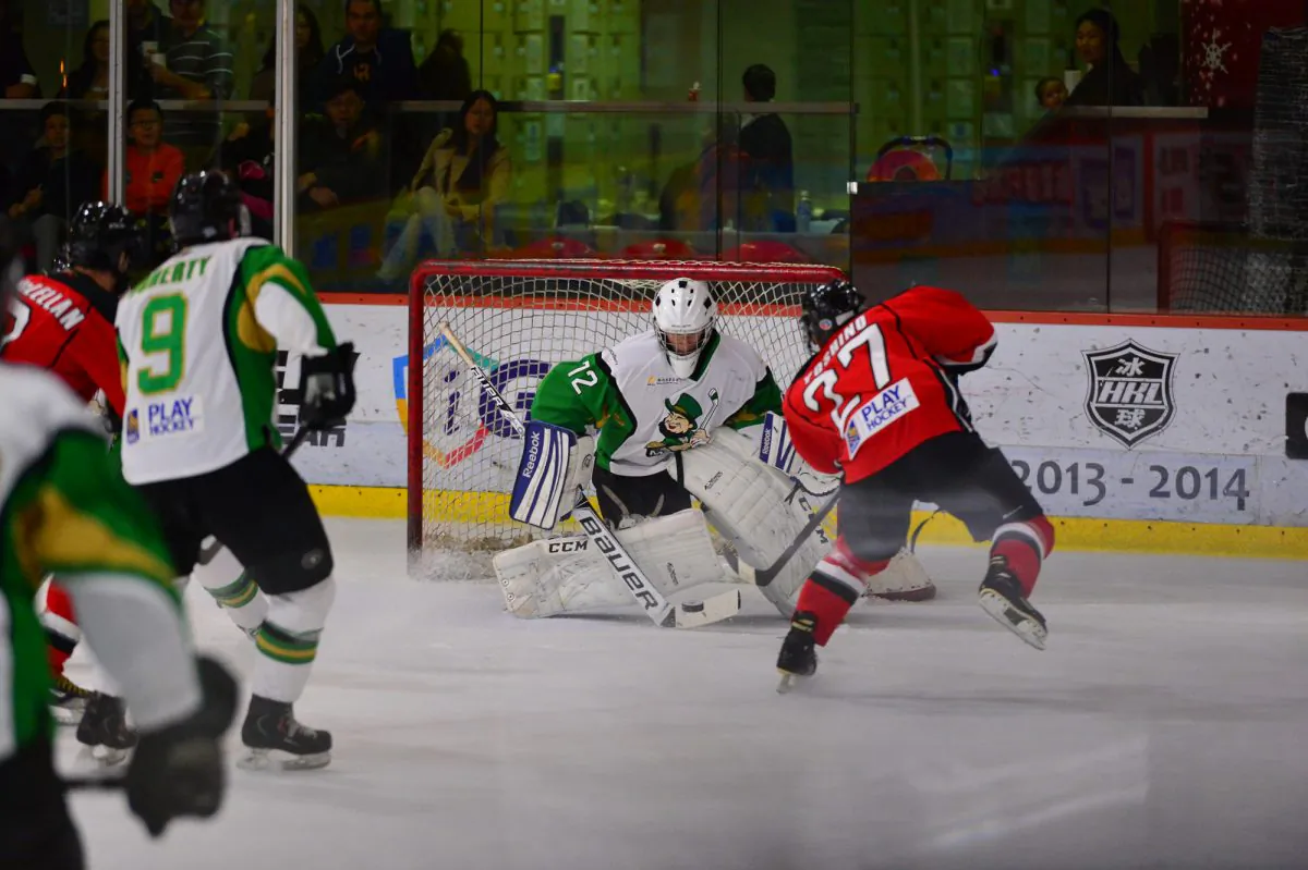 Michael Yoshino of Kowloon Warriors squeezes the puck through a very narrow gap to make the score 5-1 in Period-2 against Macau Aces in their CIHL Semi-final on Saturday Mar 8, 2014. (Bill Cox/Epoch Times)