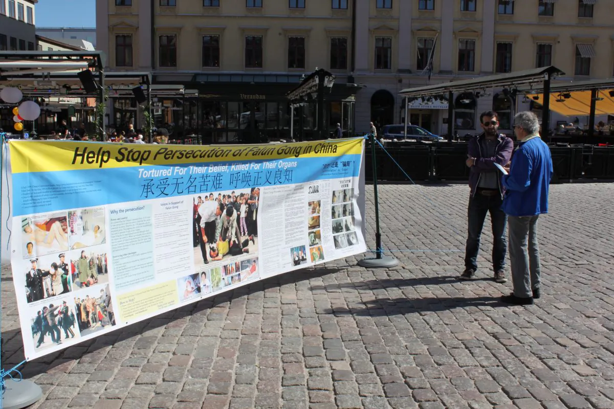 A citizen of Linkoping listens with interest as a local Falun Gong practitioner explains what Falun Dafa (also known as Falun Gong) is and how it is persecuted by the Chinese communist regime; at Stora Torget, the main square in Linkoping, Sweden, on April 26, 2014. (Epoch Times)