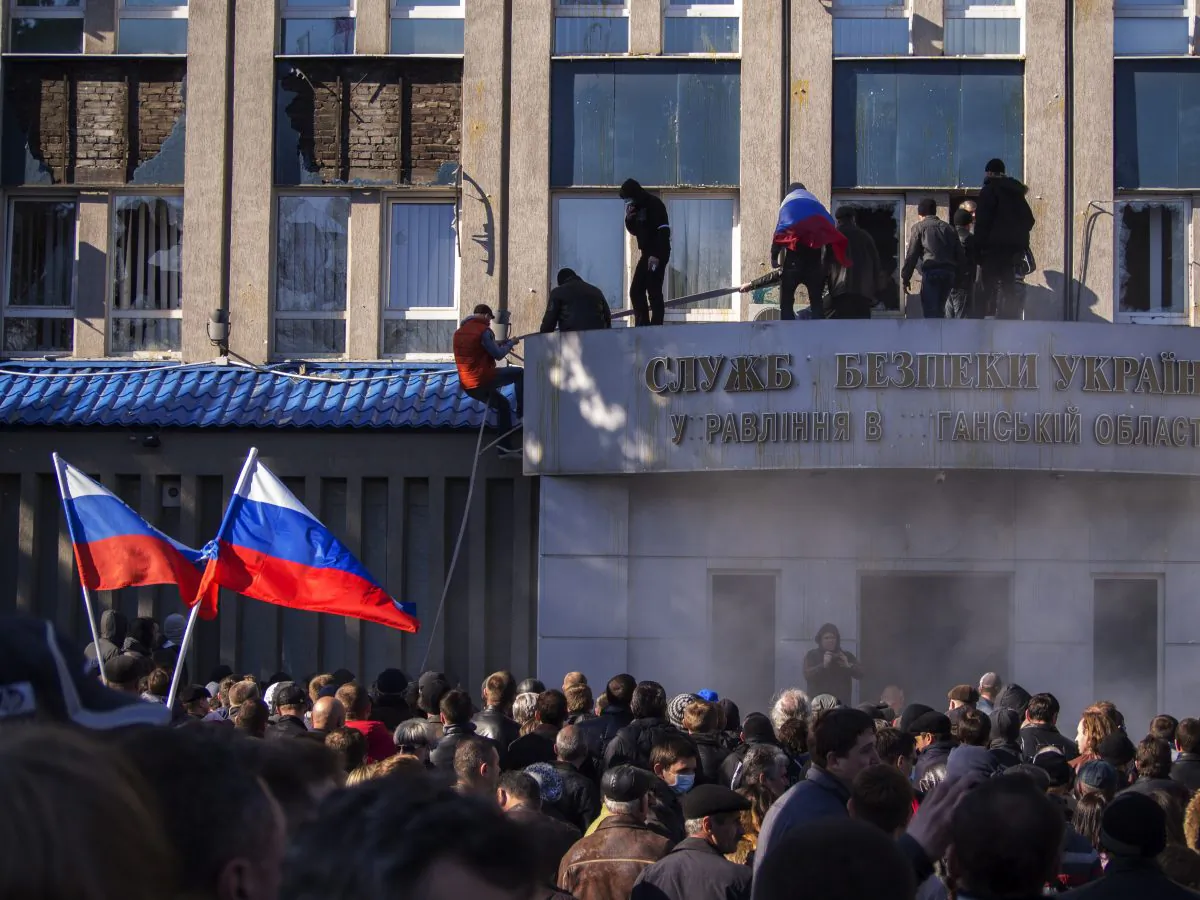 Pro-Russian activists with Russian national flags storm the Ukrainian regional office of the Security Service in Luhansk, Ukraine, on April 6, 2014. In Luhansk, 30 kilometers (20 miles) west of the Russian border, hundreds of people surrounded the local headquarters of the security service and later scaled the facade to plant a Russian flag on the roof. (AP Photo/Igor Golovniov)