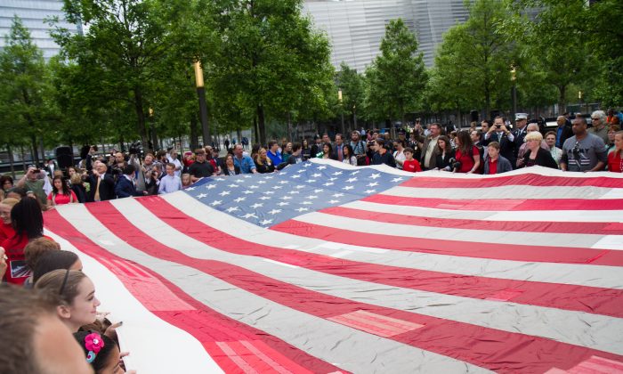 Firefighters, police and members of the public, hold the National 9/11 Flag at the ceremony for the  9/11 Memorial Museum  in New York City on Wednesday, May 21, 2014. The ceremony marked the opening of the National September 11 Memorial Museum. The flag was flying from a building near the World Trade Center on Sept. 11, 2001. It was later found shredded in the debris of ground zero and stitched back together seven years later by tornado survivors in Greensburg, Kansas.  (Benjamin Chasteen/Epoch Times)