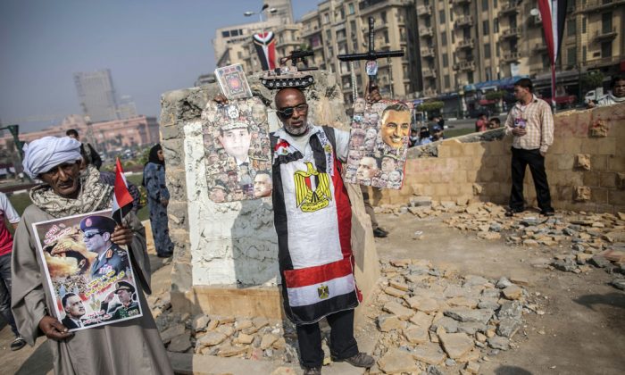 An Egyptian man dressed in the colours of his national flag and holding posters bearing images of Egypt's Defense Minister General Abdel-Fattah el-Sissi (L) and late Egyptian president Gamal Abdel Nasser (L) amongst other political leaders as protestors gather in Tahrir square to mark the anniversary of anti-military protests on November 19, 2013 in Cairo. Dozens of supporters and opponents of the army gathered in Tahrir to mark the anniversary of anti-military protests, amid mounting anger over a memorial to those killed in Egypt's uprising. (Mahmoud Khaled/AFP/Getty Images)