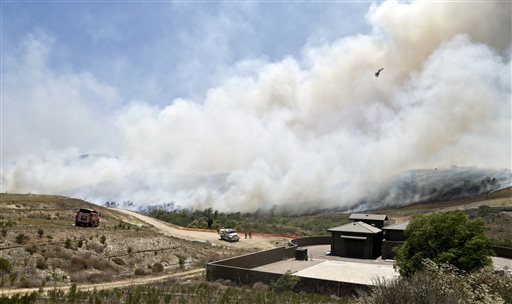 Smoke rises from a canyon where a wild fire is burning Tuesday, May 13, 2014, in San Diego. Wildfires destroyed a home and forced the evacuation of several others Tuesday in California as a high-pressure system brought unseasonable heat and gusty winds to a parched state that should be in the middle of its rainy season. (AP Photo)