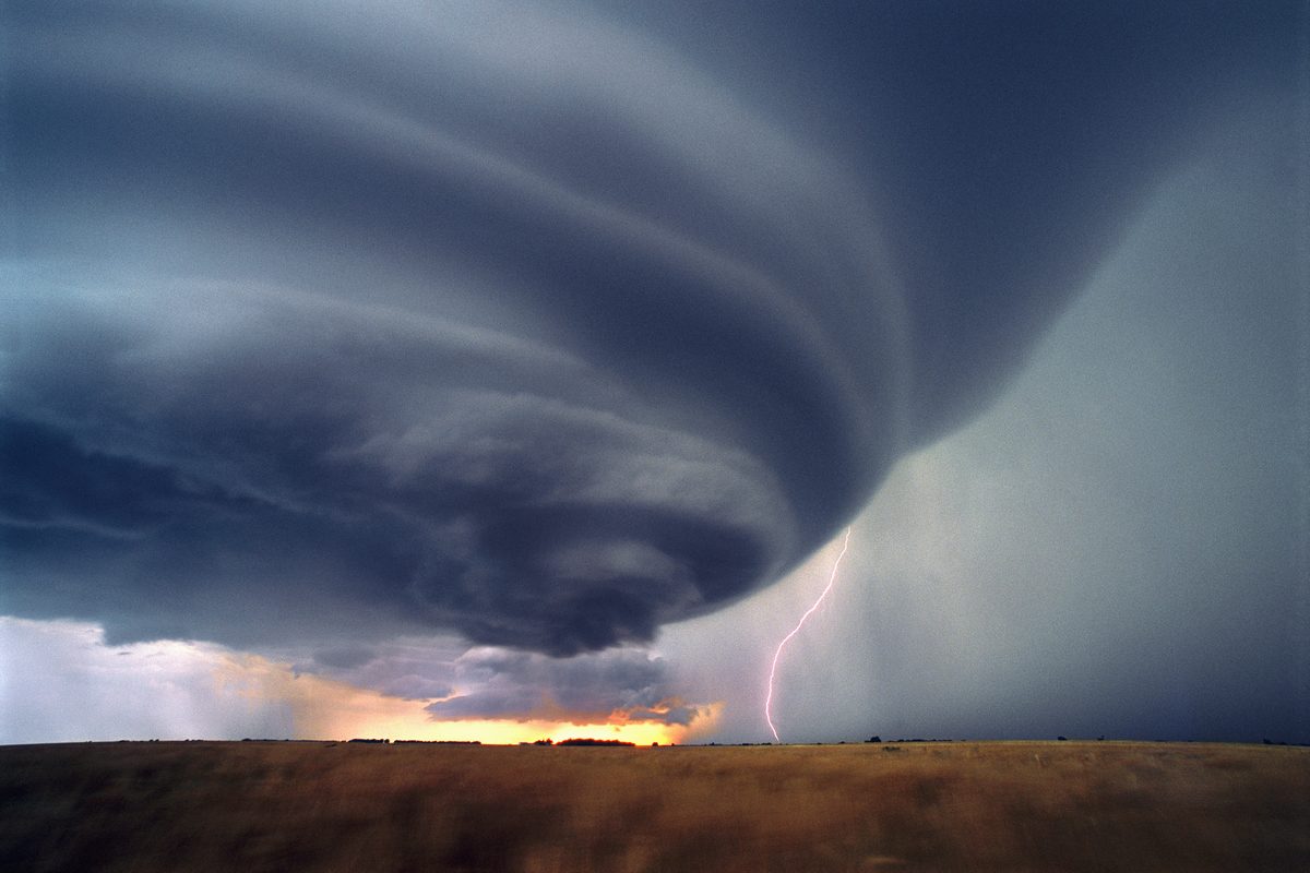 A lone lightning bolt strikes the ground beneath an isolated supercell thunderstorm at sunset. The flying saucer-shaped severe cell produced baseball-sized hailstones. (Jim Reed)