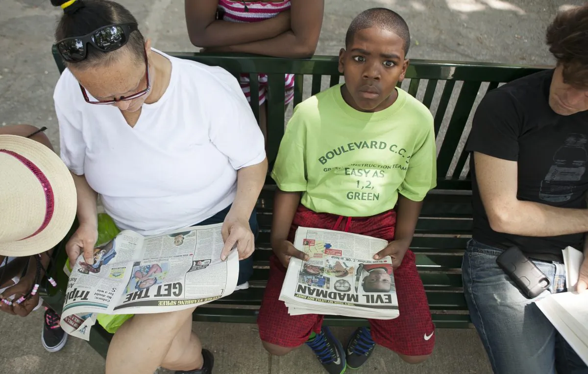 A boy looks up from a tabloid newspaper with an image of Prince Joshua Avitto, 6, a boy killed on June 1, at the Boulevard Houses project, in East New York, New York, on June 3, 2014. (Samira Bouaou/Epoch Times)