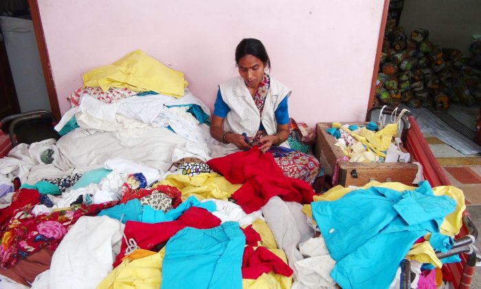 An employee of Indian NGO Goonj sits amid discarded and sorted clothes at the organization’s office in New Delhi on June 7, 2014. Goonj collects, washes, and mends discarded clothes and uses them as currency to pay poor villagers to build community infrastructure, an initiative called Clothes for Work. (Venus Upadhayaya/Epoch Times)